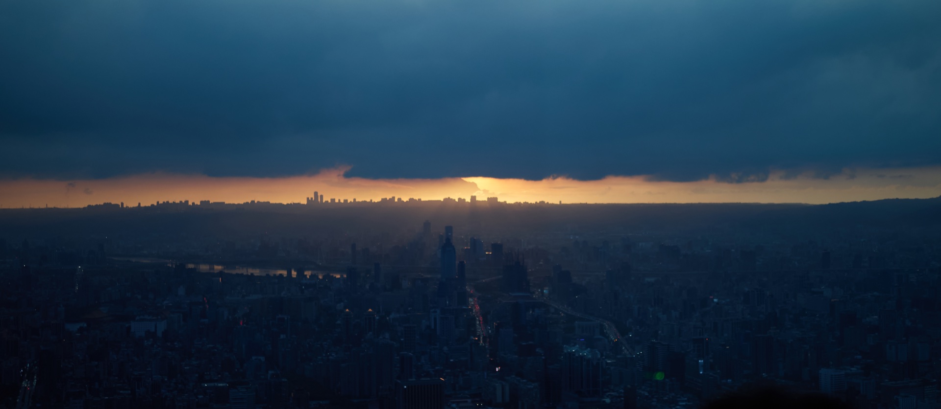 A city seen from high above as the sun sets beneath dark clouds